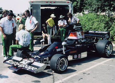 The Interscope Lola T332 at Long Beach in 1975.  Chief crew Mark Blaze is sitting on the front wheel talking with Ed O'Brien and Peter Miles; team manager Carroll Smith is at the back in his usual hat. Copyright Mark Blaze 2016. Used with permission.