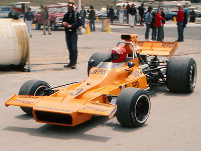 Frank Matich in his race Matich A51 in the paddock at Laguna Seca in 1973. Copyright Bob Moffett 2026. Used with permission.